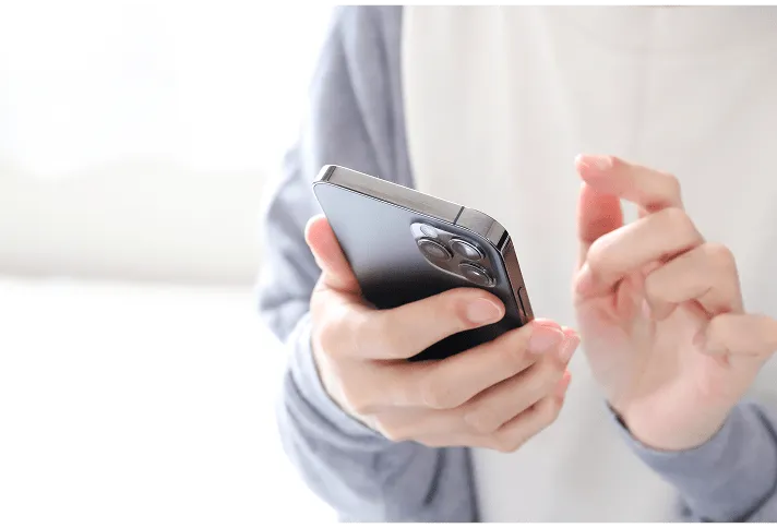 グレーの服を着た人が両手でスマートフォンを持ってタッチ操作している様子