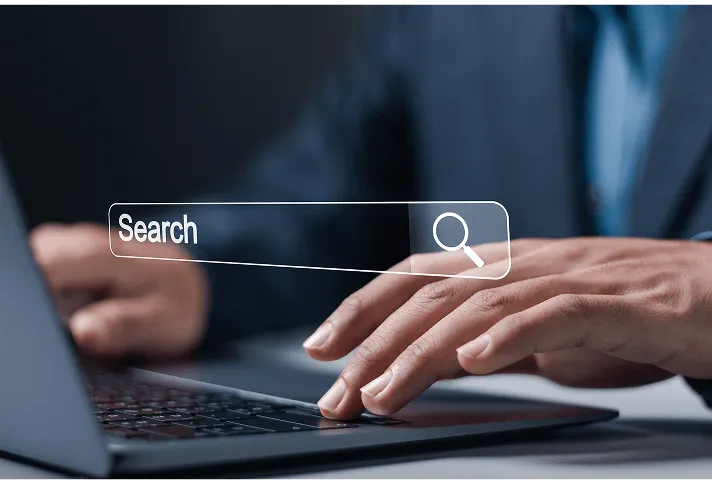 「Search」と表示された検索バーの上に手をかざしている様子、ノートパソコンのキーボードが背景にある