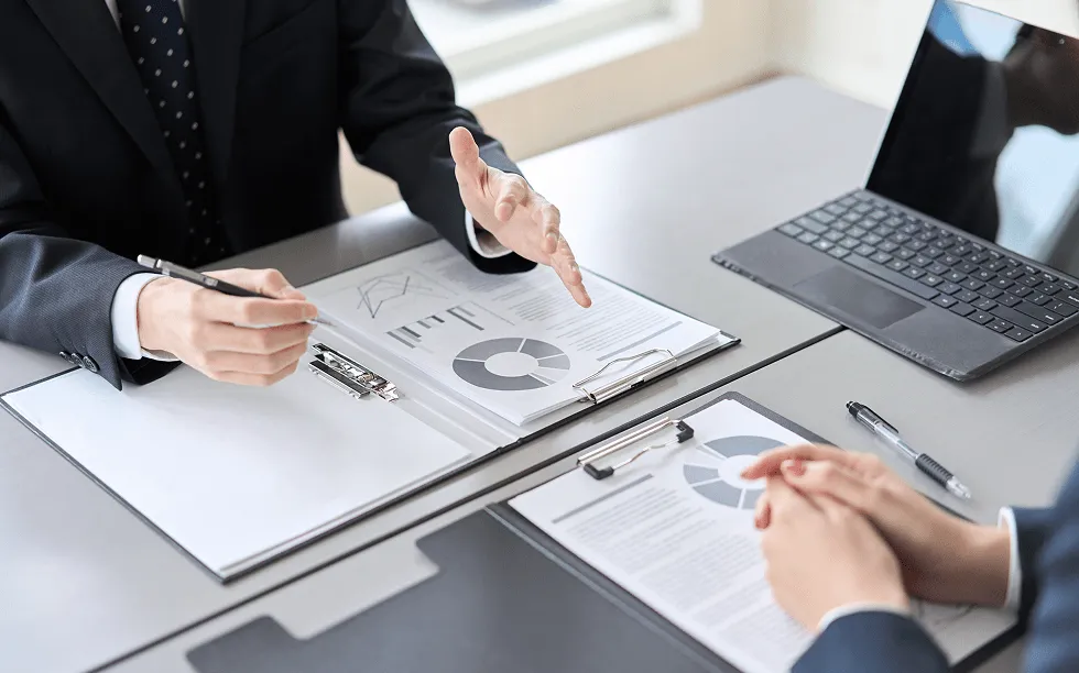 スーツ姿のビジネスパーソンが円グラフや棒グラフの資料を使って会議をしている様子